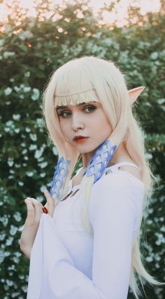 a woman with blonde hair and blue eyes is dressed up as an elf in front of some bushes