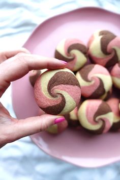 a pink plate topped with lots of brown and pink donuts on top of a table