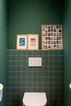 a green tiled bathroom with pictures on the wall and a toilet in the foreground