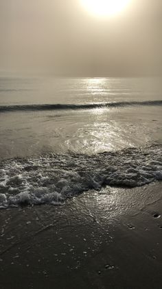 the sun is shining over the water at the beach with waves coming in to shore