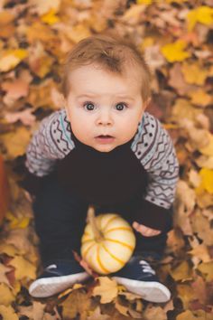 a little boy sitting on the ground with some pumpkins in his hands and looking up