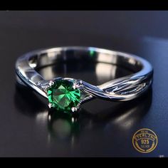 a green ring sitting on top of a black table next to a white gold band