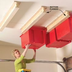 a woman standing on a step ladder holding two red bins above her head, with the bottom frame removed