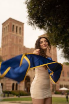 a beautiful young woman holding onto a blue and yellow scarf in front of a building