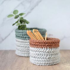 two crocheted baskets sitting next to each other on top of a wooden table