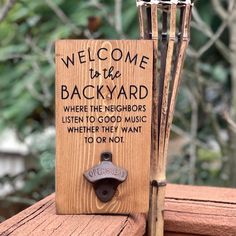 a welcome to the backyard sign on top of a wooden fence with an iron hook