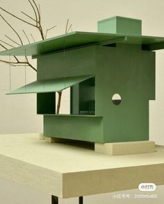 a green house sitting on top of a wooden table next to a bare tree with no leaves