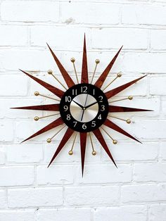 a black and red clock on a white brick wall with gold studdings around it