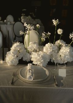 the table is set with white flowers and silverware