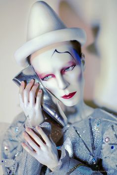 a woman with white makeup holding a silver shoe