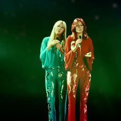 two women standing next to each other in front of a green and red background, one holding a microphone