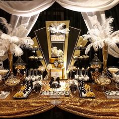 a table topped with lots of desserts covered in gold and white feathers next to a window