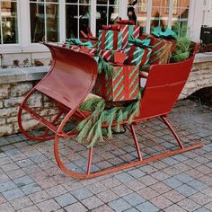 a red sleigh filled with christmas presents on top of a brick floor next to a building