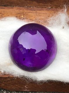 a large purple ball sitting on top of white wool next to a piece of wood