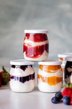 four jars filled with fruit and yogurt sitting on a table next to strawberries