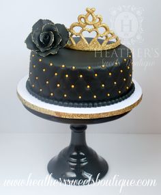 a black and gold decorated cake with a rose on top is sitting on a pedestal