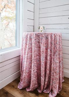 a table with a pink cloth draped over it in front of a white wall and window