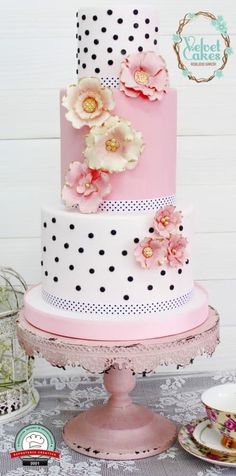 a three tiered cake with polka dots and flowers on top is sitting on a table