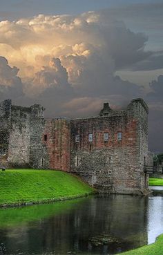 an old castle sitting on top of a lush green field next to a body of water