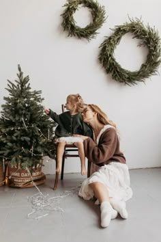 a woman and child sitting in front of a christmas tree with wreaths on the wall