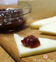 cheese slices with jam on them sit on a cutting board next to a glass bowl