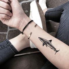 a person with a shark tattoo on their arm holding onto the wrist and another hand