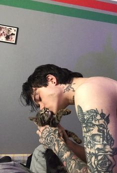 a man with tattoos holding a cat in his hands