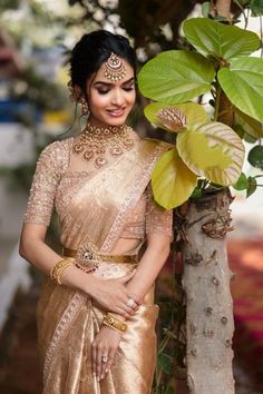 a woman in a gold sari standing next to a tree