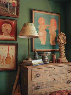 an old dresser with two lamps and paintings on the wall in a green living room