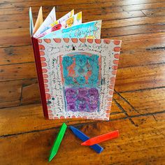 an open book sitting on top of a wooden table next to colored crayons