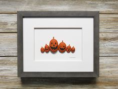 three pumpkins with faces cut out of them in a shadow box frame on a wooden surface