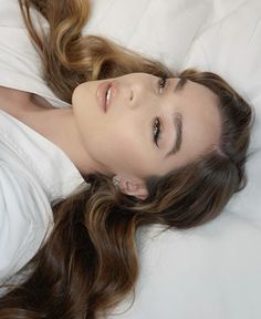 a woman laying on top of a white bed covered in sheets and pillows with her eyes closed