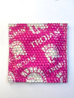 pink and white beaded square with flowers on the bottom, in front of a white wall