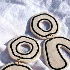 two pairs of white and black earrings on top of a white cloth covered tablecloth