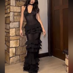 a woman standing in front of a door wearing a black dress with ruffles