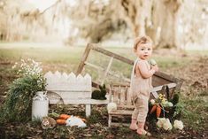 a toddler standing in front of a wooden bench with flowers and greenery on the ground