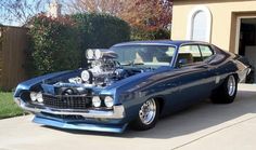 an old muscle car parked in front of a house with the hood up and engine on