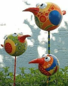 three colorful birds sitting on top of green plants