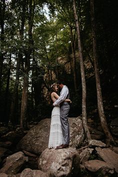 a bride and groom standing on rocks in the woods