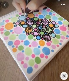 a person is drawing on a notebook with colored polka dot paper and marker pens while sitting at a table