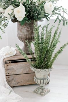 two vases with white flowers and greenery in them