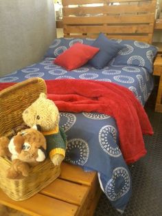 two teddy bears sitting in a wicker basket on top of a wooden table next to a bed