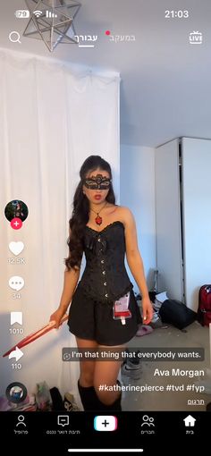 a woman in a black corset and mask holding a red stick while standing next to a white wall