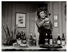 an older woman standing in front of a table filled with wine bottles