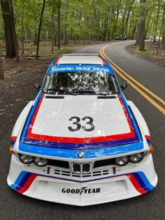 a white and blue car parked on the side of a road in front of trees