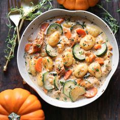 a white bowl filled with chicken and veggies next to pumpkins on a wooden table