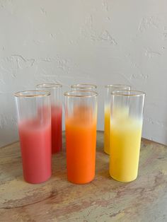 four glasses with different colored liquids sitting on a table