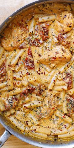 a skillet filled with pasta and sauce on top of a wooden table