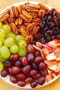 a white plate topped with grapes, pecans and nuts next to fruit on top of a wooden table