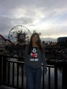 a woman standing in front of a ferris wheel with mickey mouse on her t - shirt